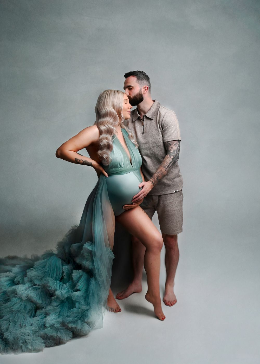 Maternity photoshoot featuring teal fabric and couple poses against neutral backdrop.