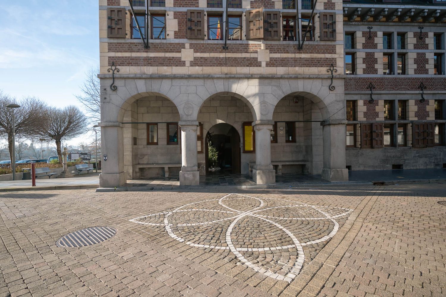 Ornate stone archway entrance of historic building with brick pavement and geometric chalk art pattern on ground.