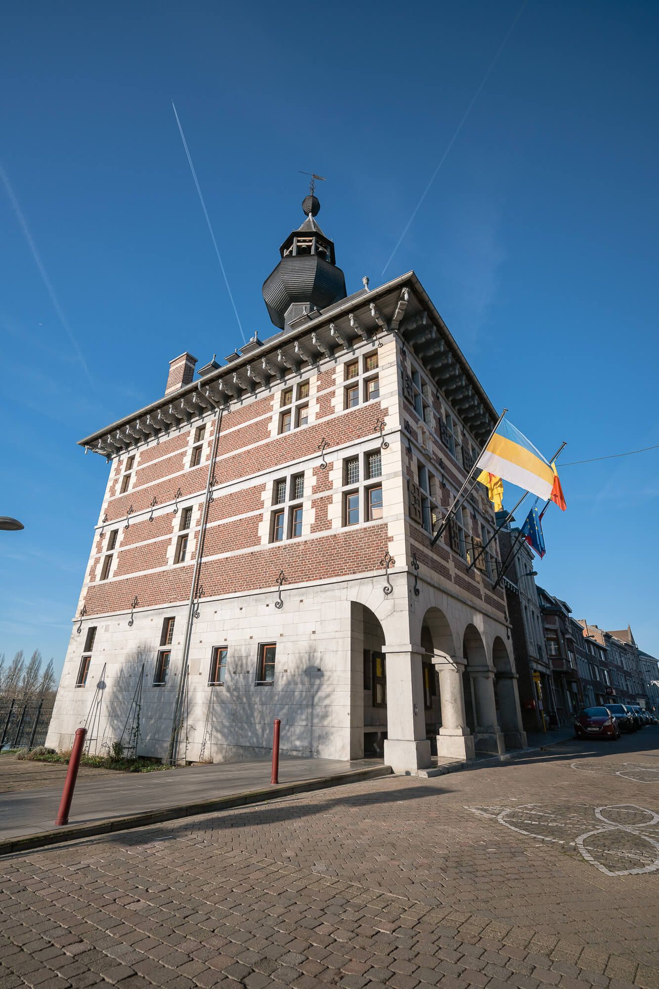 Different perspectives of a traditional Belgian brick building with white trim and a distinctive black cupola on its roof.