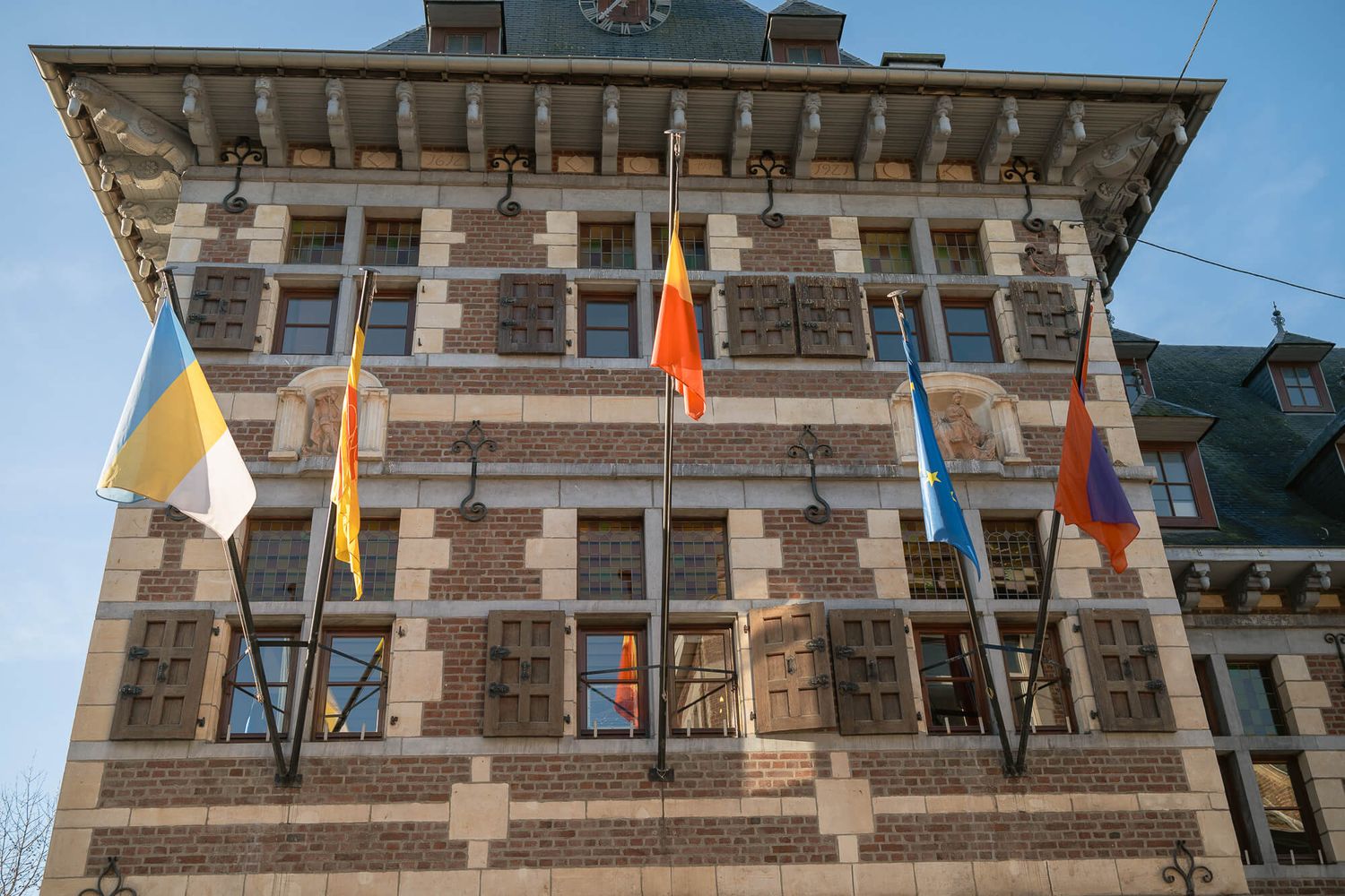 Historic brick building with striped stone facade and colorful flags mounted along its exterior in daylight.