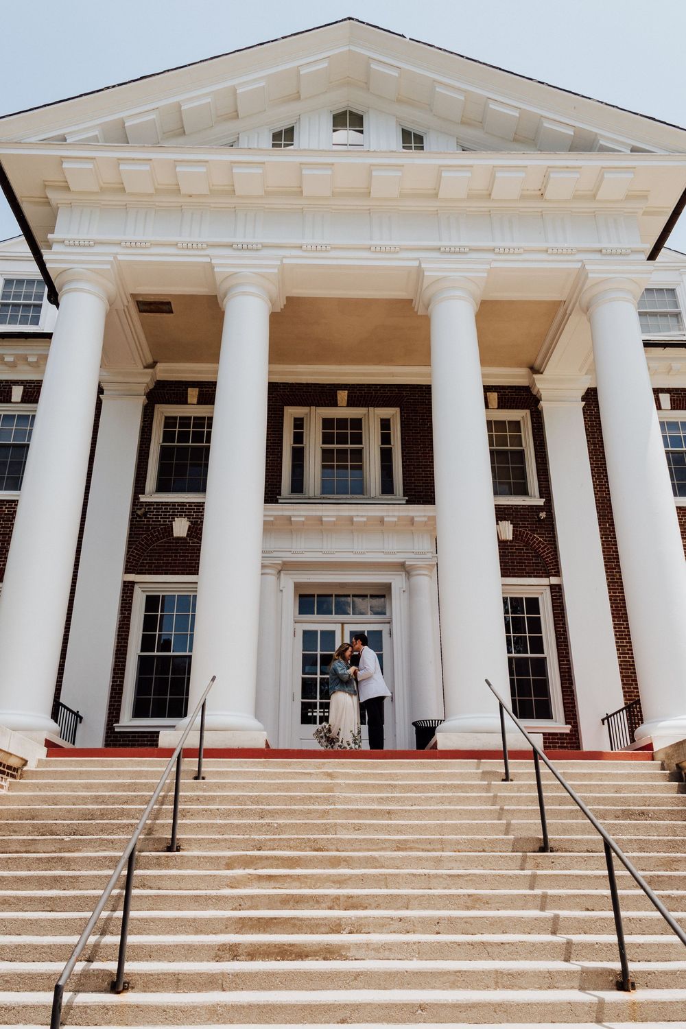 A couple posing by grand white-columned entrance with wide stone steps for engagement photos in Gettysburg College.