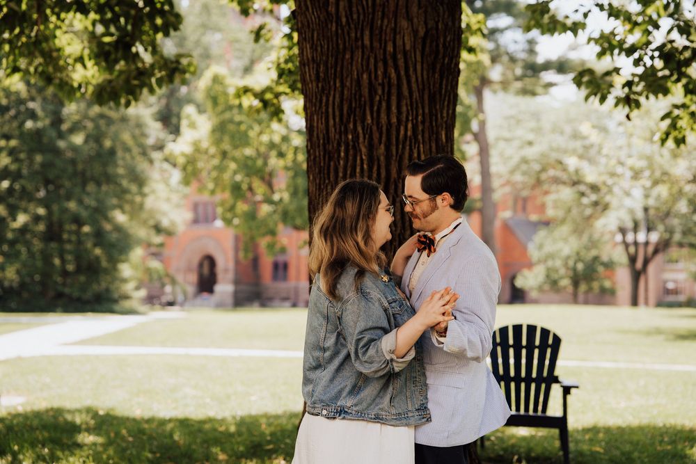 A couple shares an intimate embrace under trees on a sunny afternoon at Gettysburg College for engagement photoshoot.
