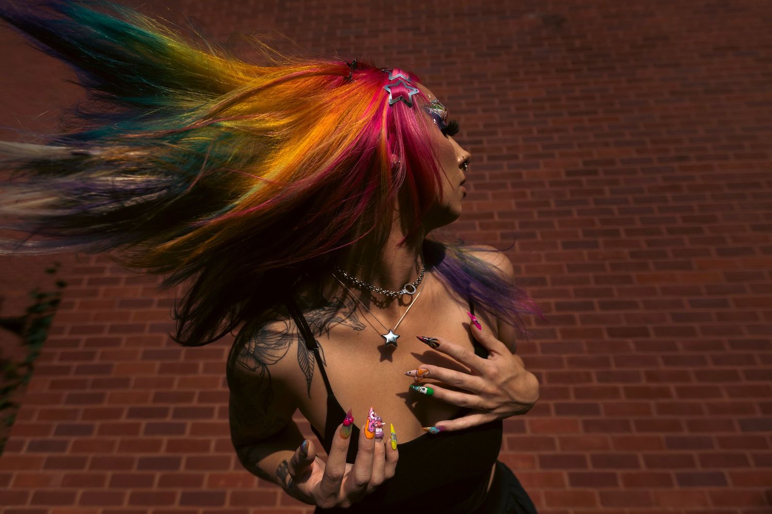 Side profile figure with vibrant rainbow colored hair whips their head against brick wall in dramatic motion.