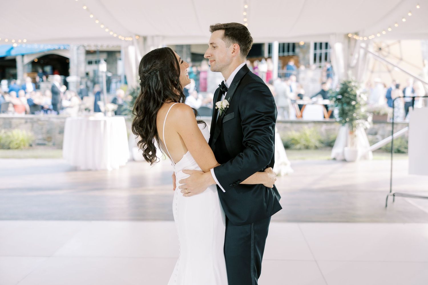A couple shares their first dance under white string lights at an elegant outdoor wedding reception.