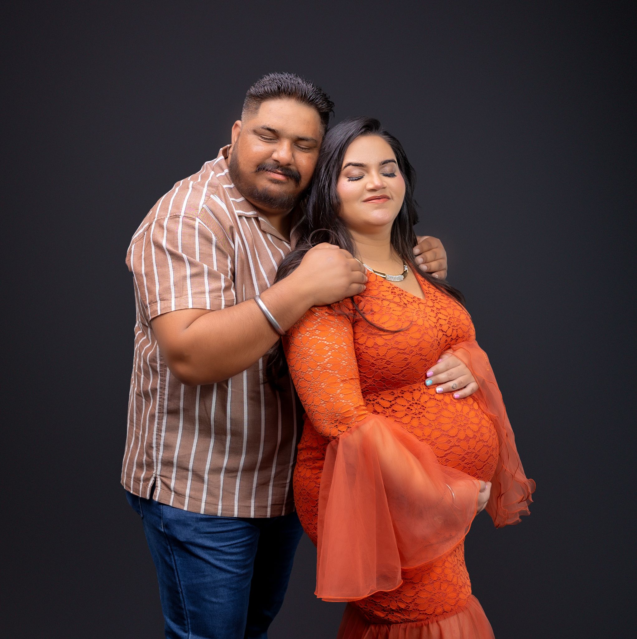 Couple posing together against dark background, with person in orange top and striped shirt.