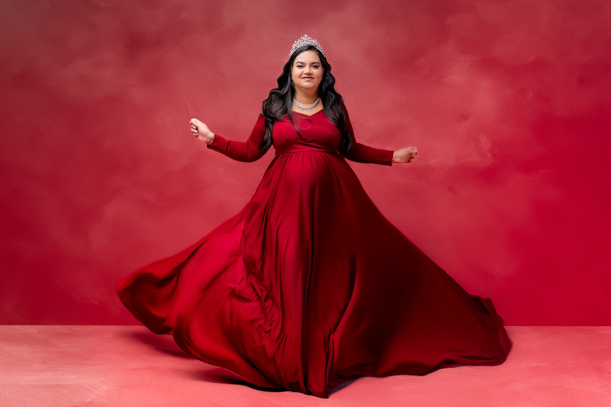 Elegant figure in a flowing red gown stands gracefully against a red background with dramatic fabric movement.