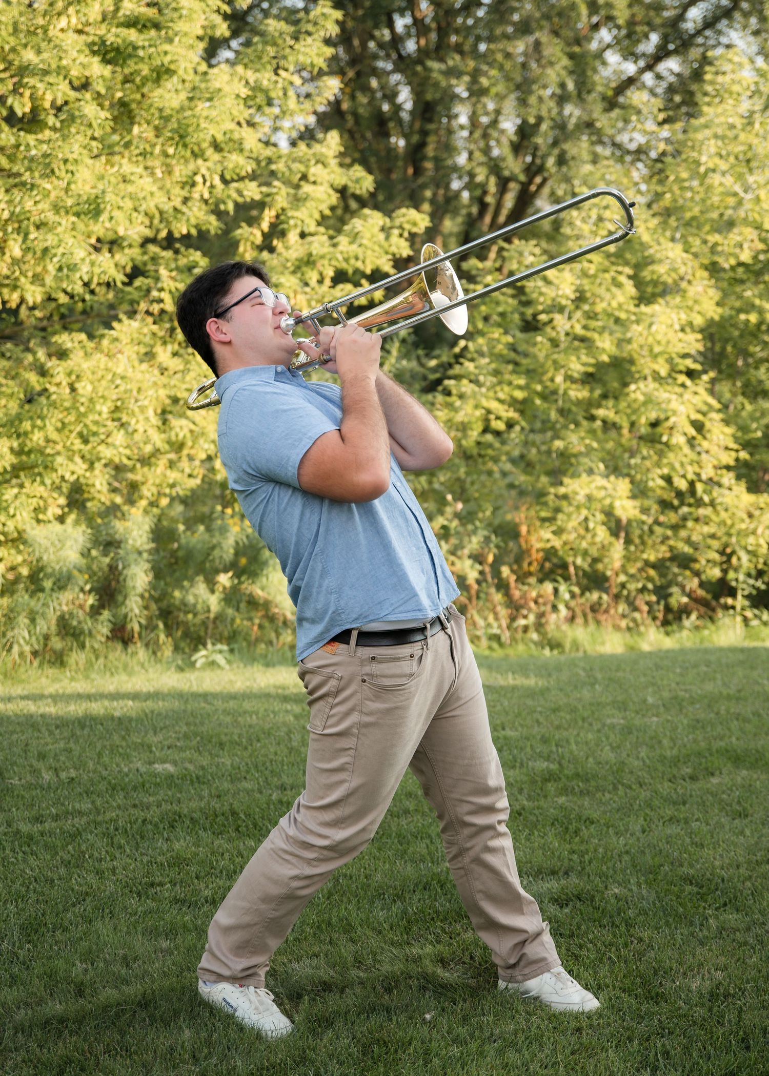 Golfer in a light blue shirt and khaki pants demonstrates a trombone solo swing sequence on a grassy hill.