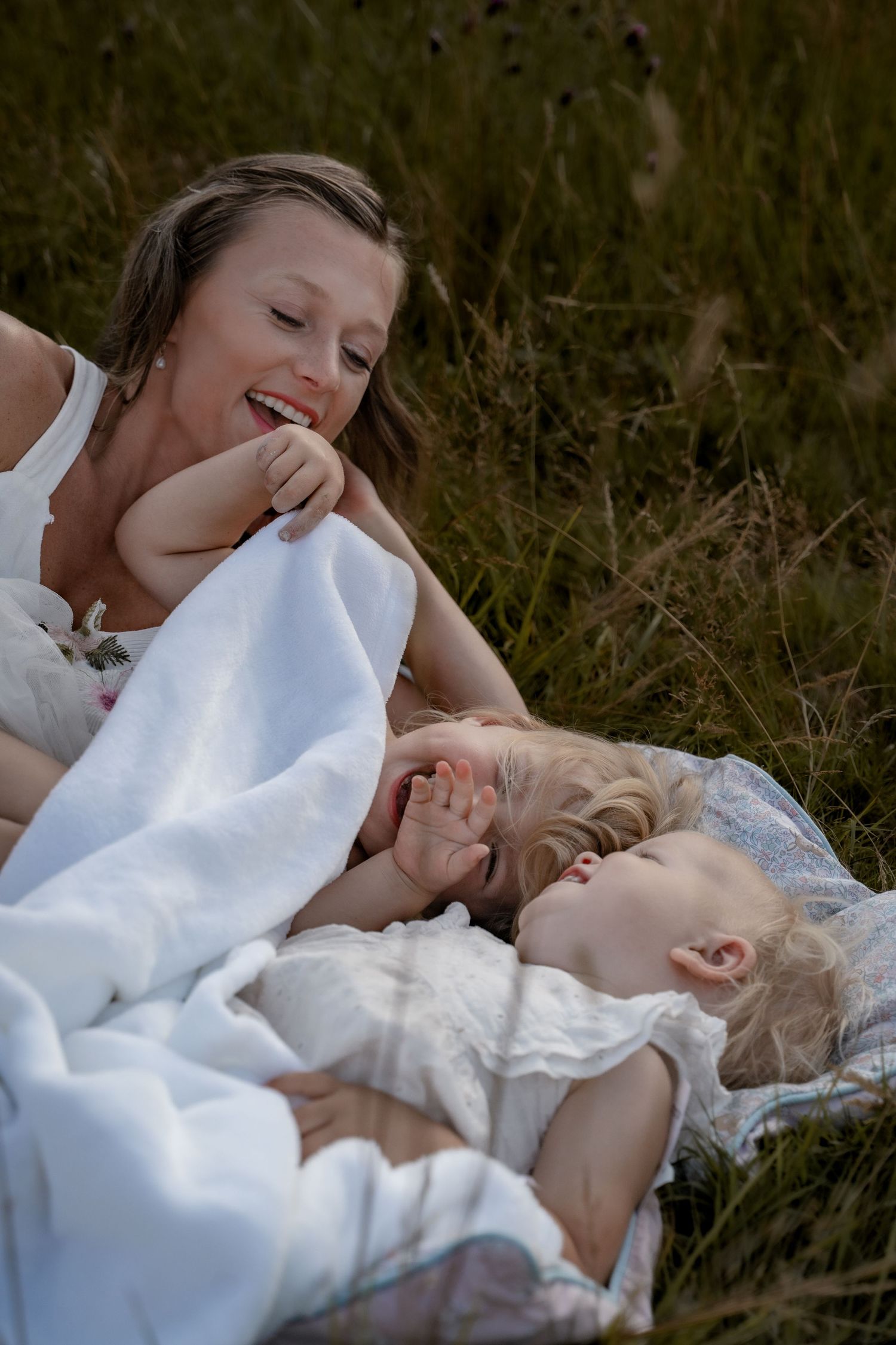 Mother laughing and snuggling with her two young children under a blanket during a relaxed outdoor motherhood photography session in Derbysh