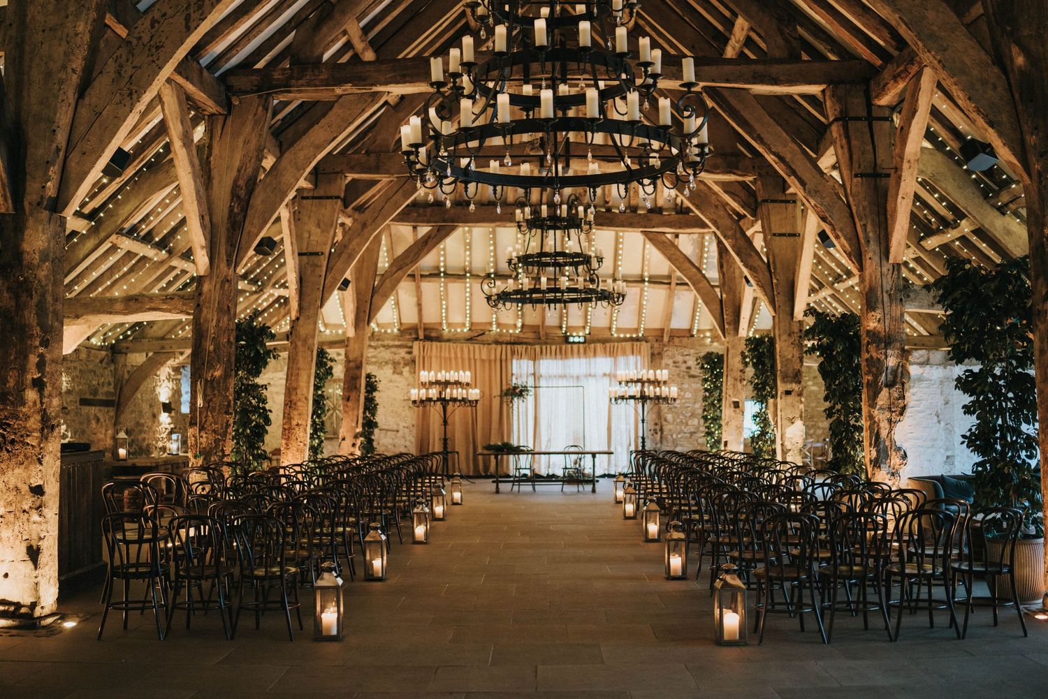 A rustic barn venue interior with exposed wooden beams and crystal chandeliers creating an elegant ambiance.
