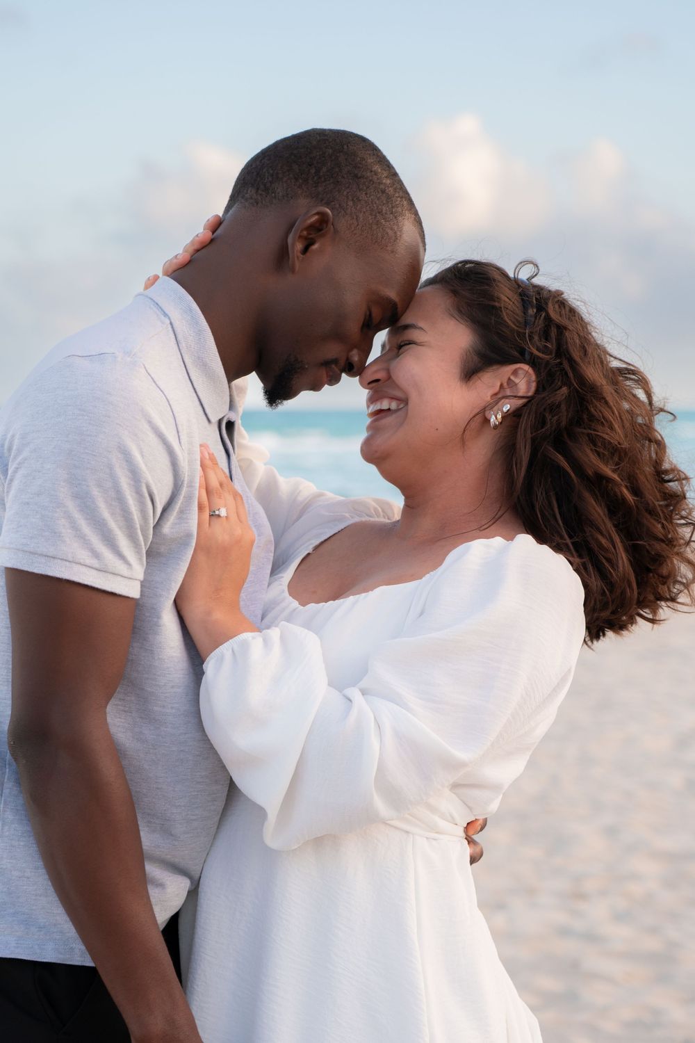 Romantic interracial couple touching foreheads and smiling on a sunny beach.