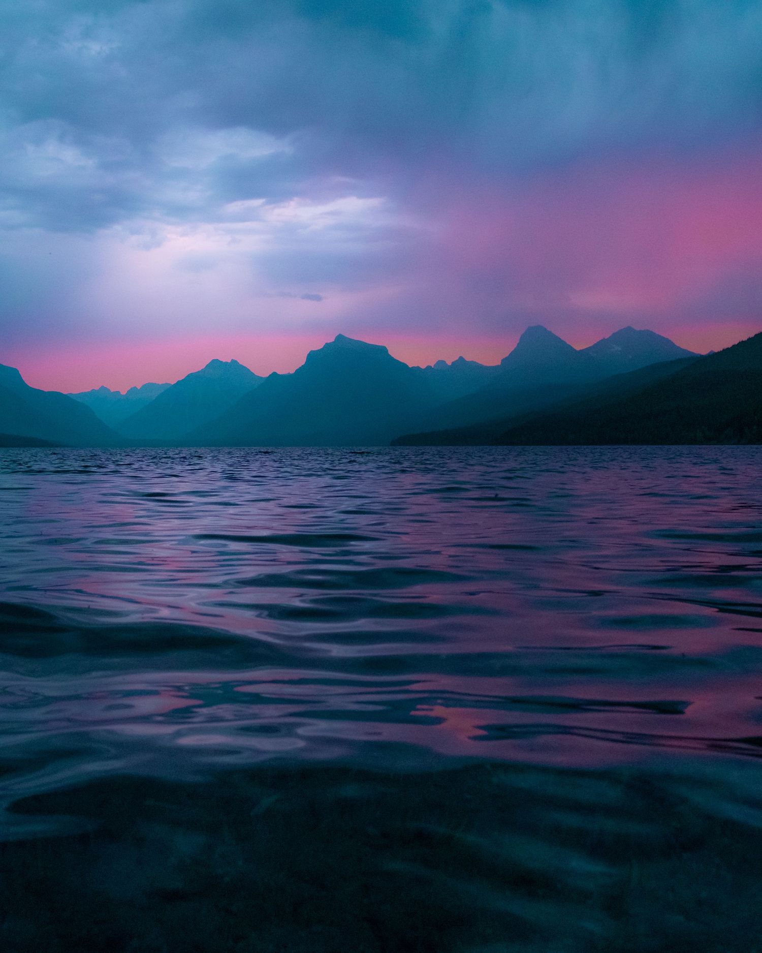 Moody sunset over mountain lake with silhouetted peaks and purple-pink sky.