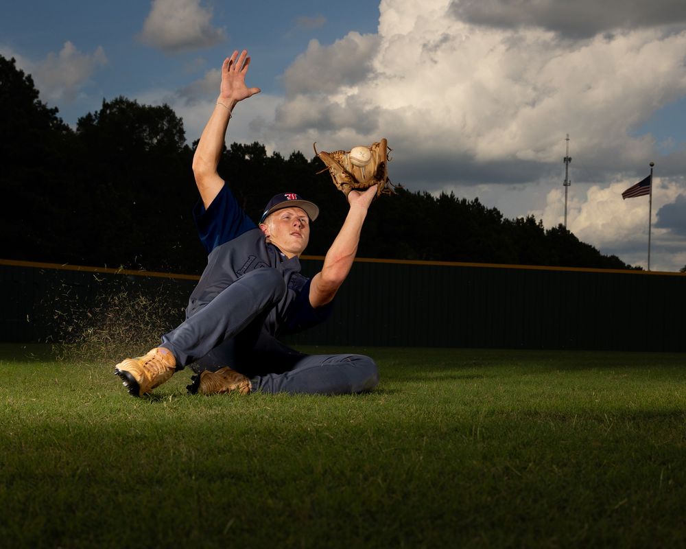 Player diving and rolling to catch a baseball in grass field against cloudy sky.