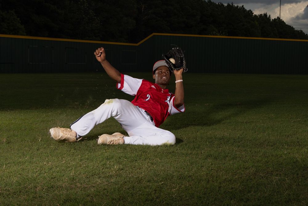 Baseball player makes dramatic sliding catch in green grass outfield during game action.
