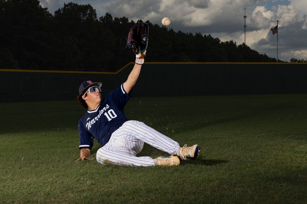 Baseball player in white and navy uniform makes dramatic sliding catch in outfield grass.