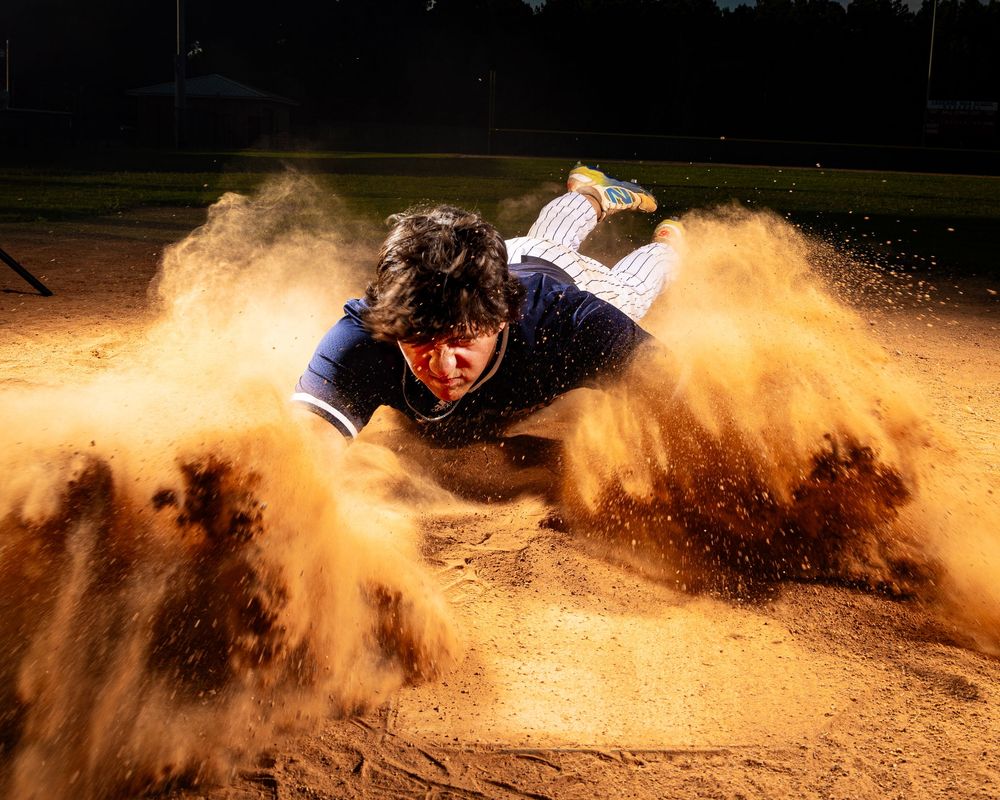 Motocross rider kicks up dramatic clouds of orange dirt while racing through a winding dirt track during competition.