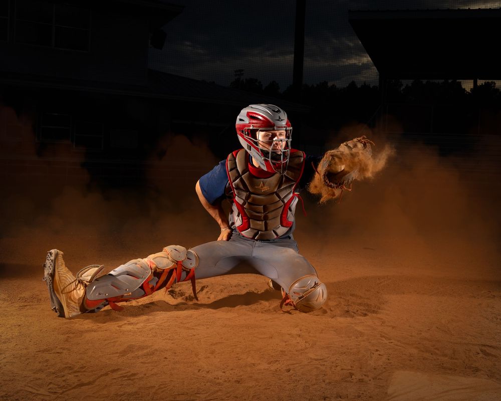Baseball players slide into home plate during an intense night game as dust clouds rise from the dirt infield.