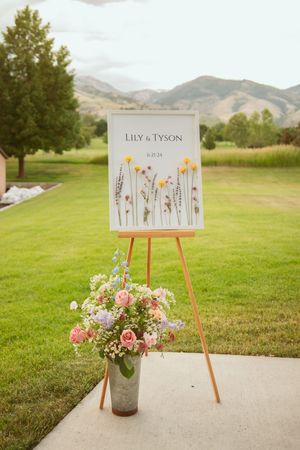 Wedding seating chart on wooden easels displays floral design details against mountain landscape backdrop.