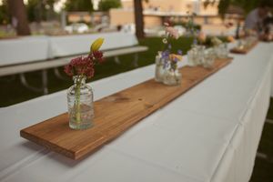 Simple rustic wedding table decor with wooden planks and small glass vases filled with pink flowers lined up together.