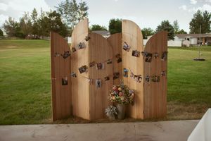 A rustic curved wooden privacy screen with decorative iron hinges stands on grass in an outdoor setting.