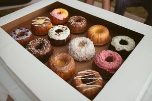 Assorted gourmet donuts with chocolate, vanilla, and strawberry glazes arranged in white bakery boxes.