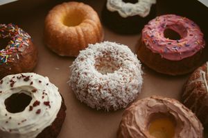 Assorted gourmet donuts with various toppings including chocolate, coconut, and sprinkles on brown surface.