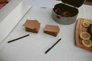 Stacks of milk chocolate bars and chocolate sticks arranged on a white surface next to lemon slices on a wooden board.