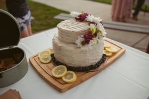 Single-tier white frosted cake decorated with fresh flowers and lemon slices on a wooden serving board.