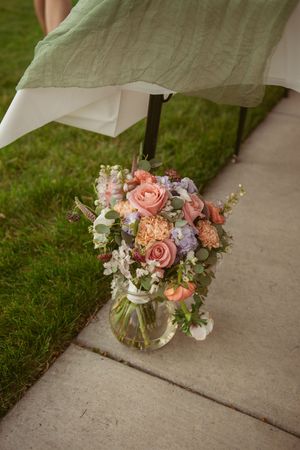 Beautiful floral arrangement in soft pink and peach tones with roses and delicate greenery rests in a glass vase.
