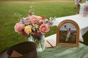 Beautiful floral arrangement with pink roses and peach carnations next to a small framed religious icon on a green tablecloth.