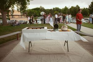 A white tablecloth covers a folding table at an outdoor community gathering with people milling about in the background.