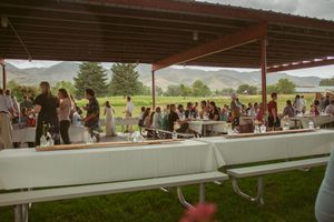 Large group of guests gathered under a covered outdoor pavilion at a ranch event during daytime.