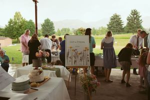 Guests gather under an outdoor pavilion at a celebration event with decorative signage and tables set up.