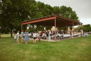 Rustic outdoor venue with wooden shelter and scattered picnic tables on a grassy hillside during an event.