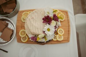 A decorated cake on a wooden board garnished with fresh lemon slices and colorful daisies and purple flowers.