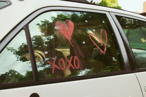 Red XOXO and heart decorations drawn on a car window creating a romantic Valentine's Day display.