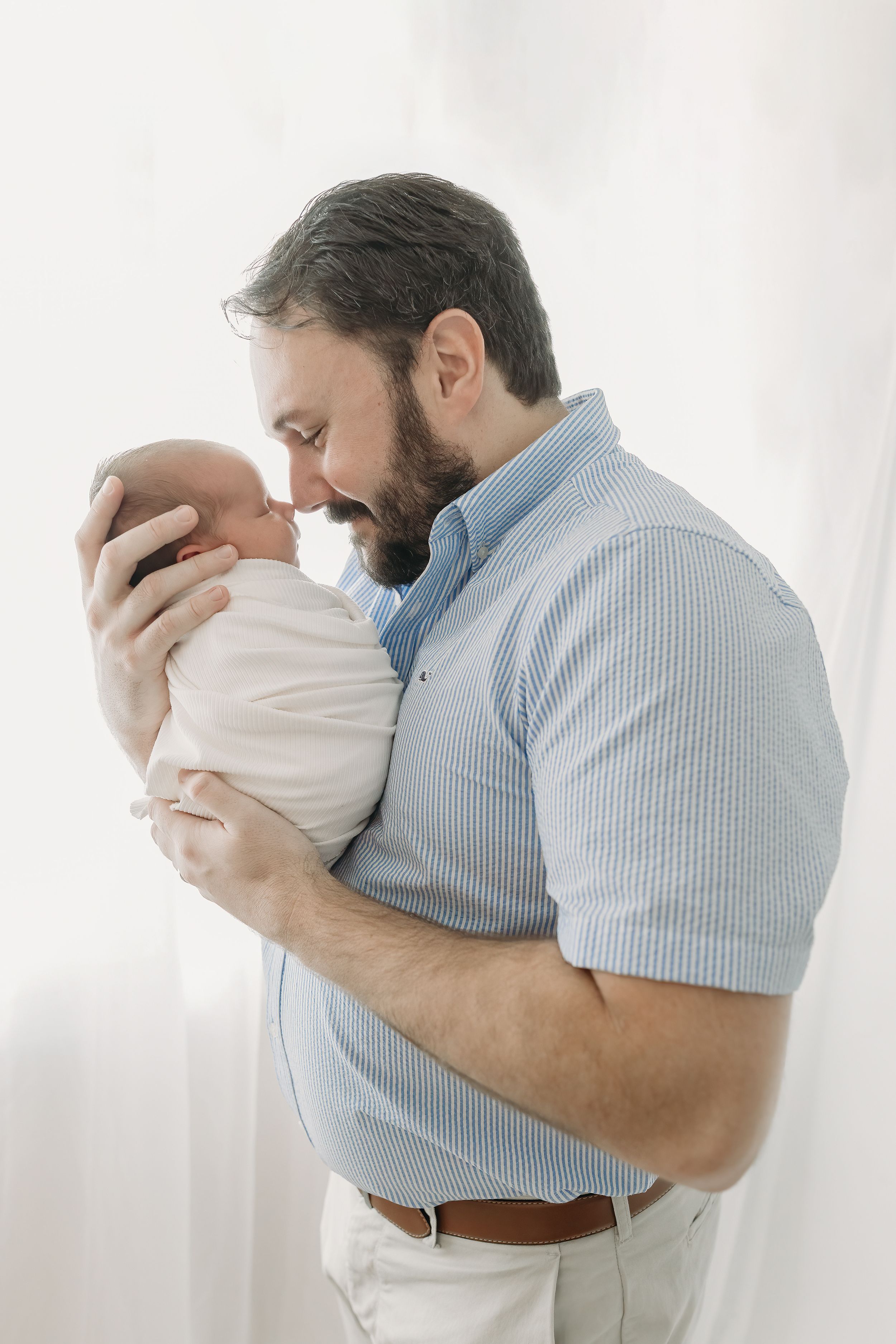 A touching moment shows a parent cradling a newborn baby wrapped in white against a bright background.