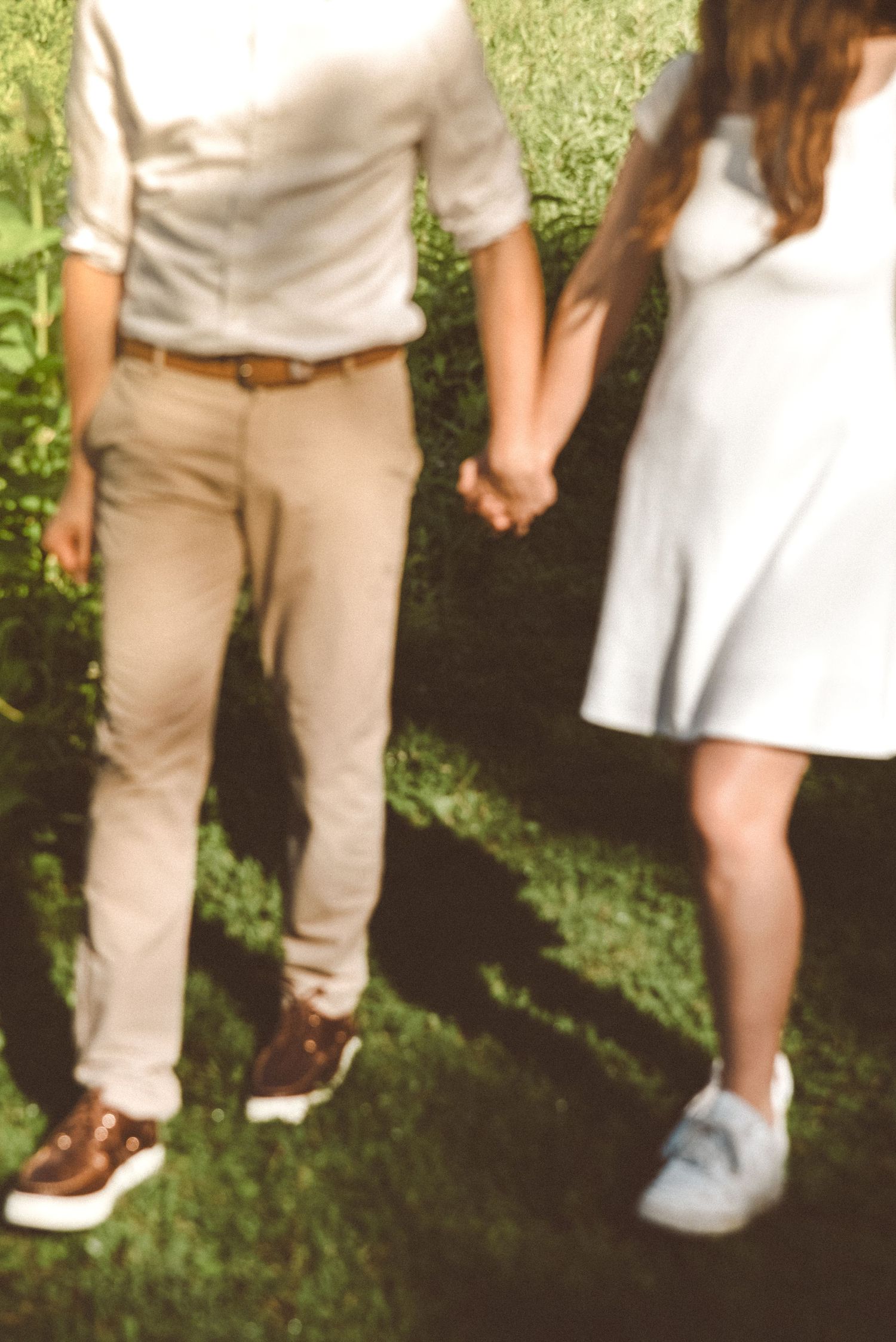 A blurry image of a couple holding hands as they walk through a grassy area.