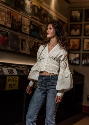 Person wearing white cropped blouse with balloon sleeves and blue jeans browses vinyl records in moody record store.