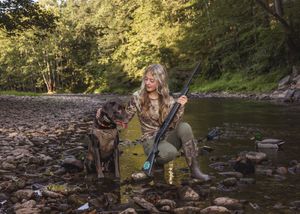 Outdoor adventure scene with camping and fishing gear along a rocky riverbank.