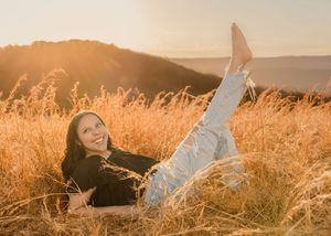 Person lying in tall golden grass during sunset with mountains in background.