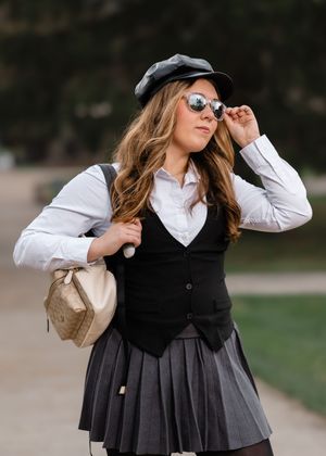 Fashion portraits in pleated skirt, vest and white shirt with sunglasses and hat outdoors.