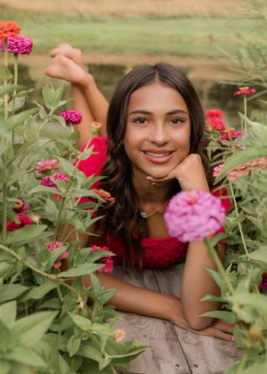 Pink zinnia flowers bloom in a garden with someone posing among the vibrant blossoms.