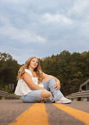 Person in blue jeans and white top lying casually on yellow road lines creating an artistic perspective shot.