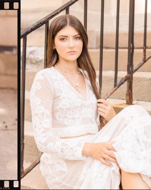 A person in a white lace dress poses thoughtfully on outdoor steps in a soft sepia-toned portrait series.