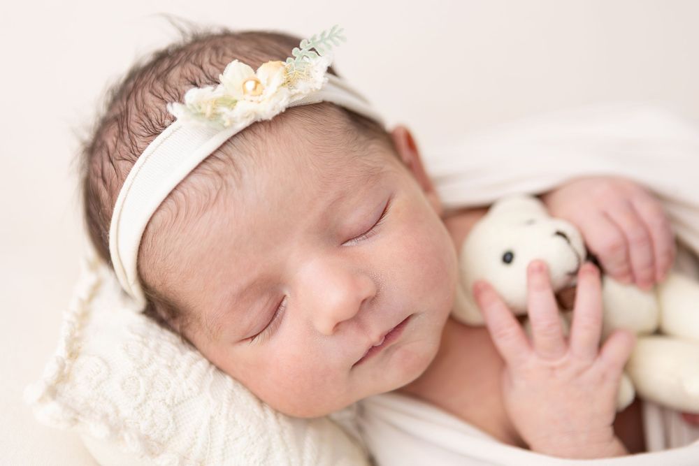 A sleeping newborn baby wrapped in soft white fabric lays peacefully with closed eyes.