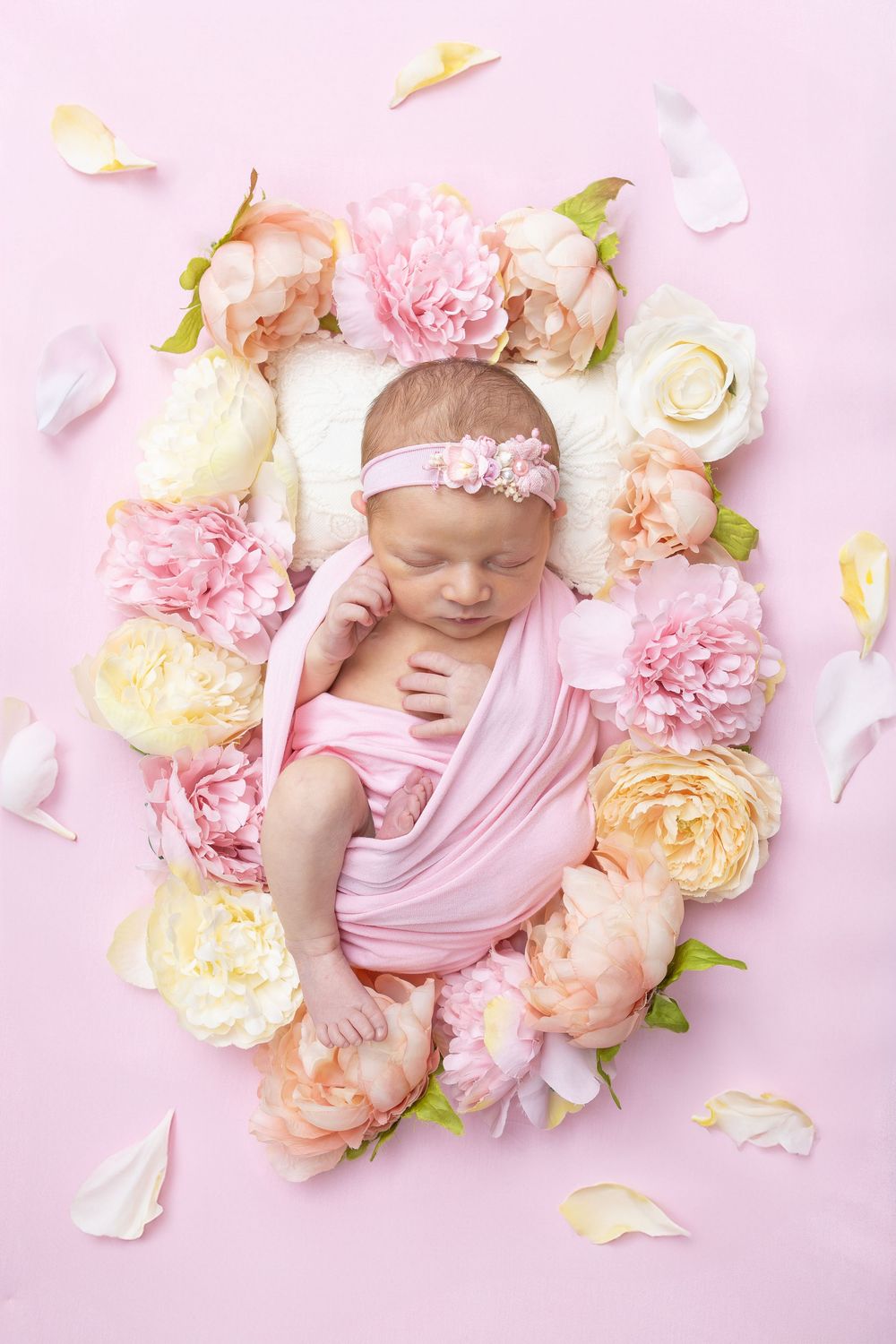 Newborn baby surrounded by pink and peach peonies on soft pink background.