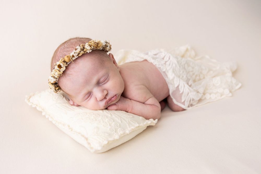 Newborn baby sleeping peacefully on white textured pillow in soft natural light.