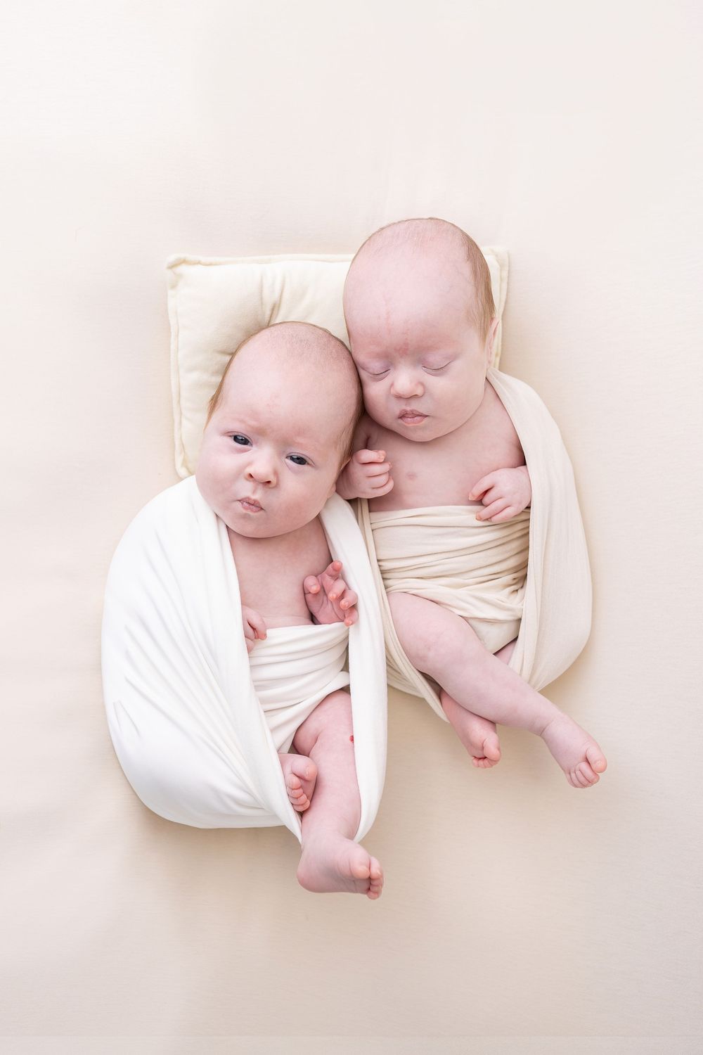 Twin newborns sleeping peacefully together wrapped in white fabric.