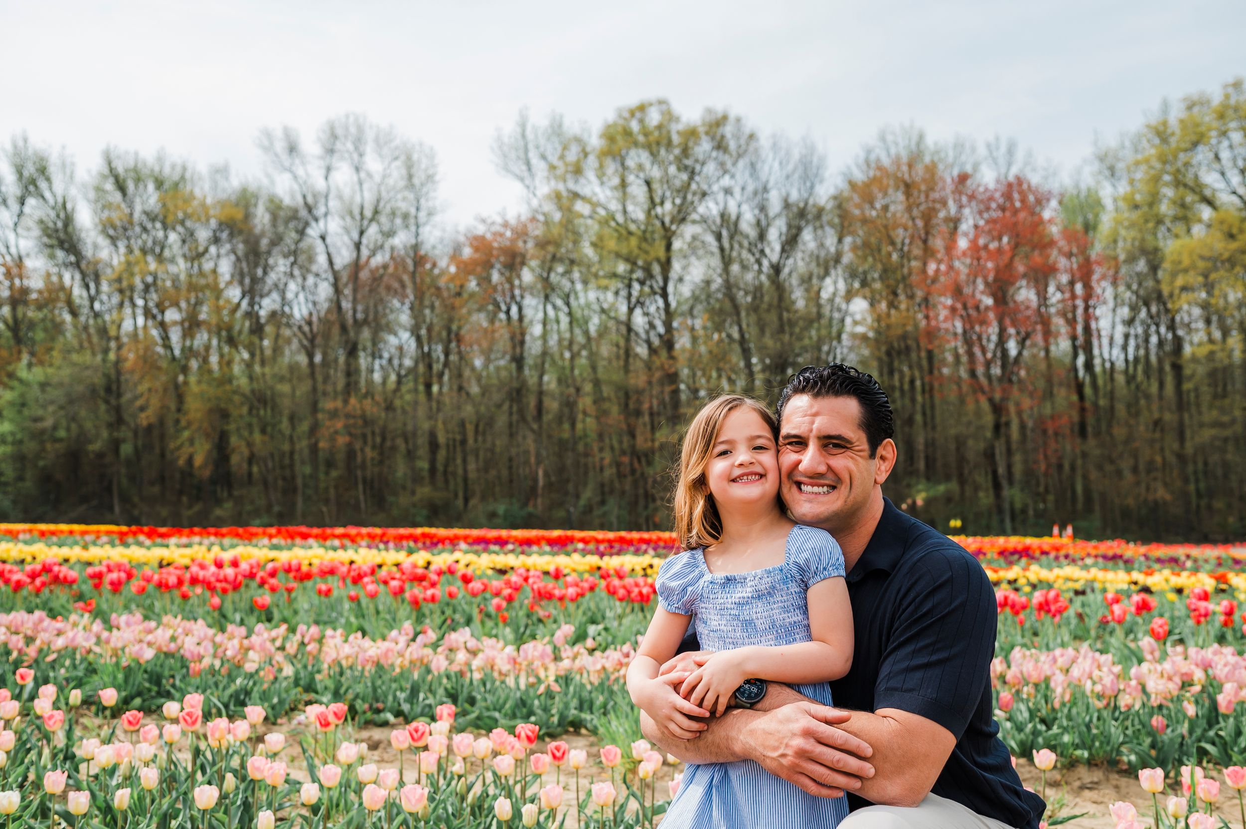 Romantic couple share laughter while sitting together in a vibrant spring tulip field filled with colorful blooms.