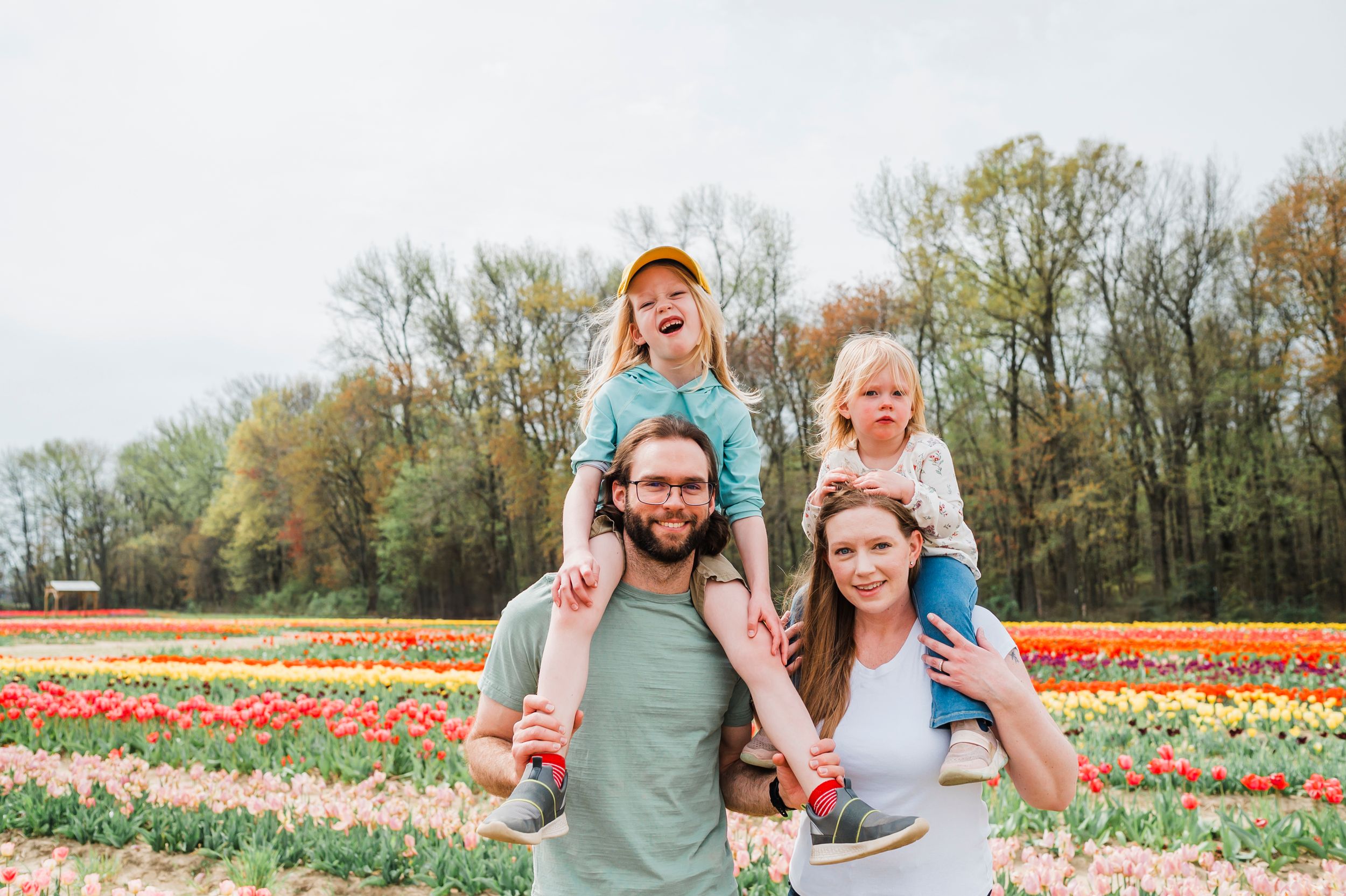 A family smiles and laughs together in a colorful springtime tulip field during a sunny afternoon.